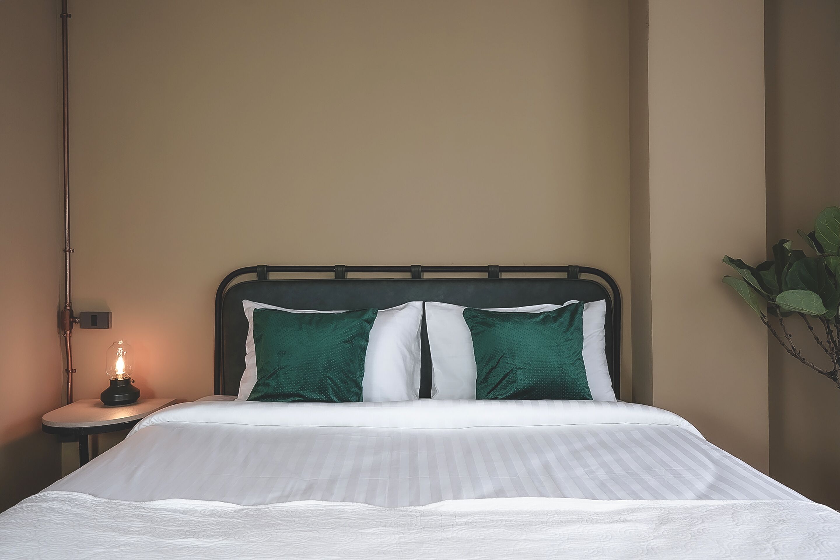 A neatly made bed with white and green pillows, a bedside lamp, and a small table with a lamp.