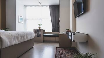 A modern bedroom with a bed, a TV mounted on the wall, a window with curtains, and a small plant on the windowsill.
