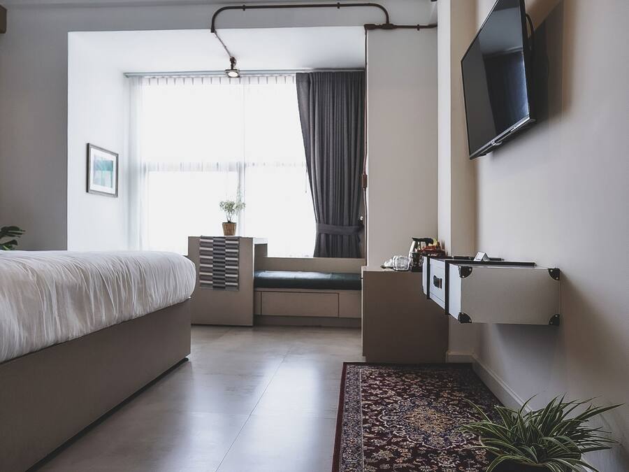A modern bedroom with a bed, a TV mounted on the wall, a window with curtains, and a small plant on the windowsill.