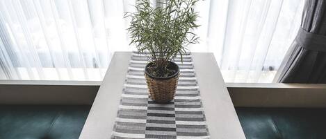 Una planta en maceta sobre una mesa a rayas en una habitación con ventana y asientos tapizados en verde.