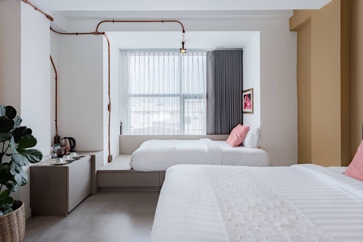 Una habitación de hotel moderna con una banca integrada, un ventanal con cortinas, una mesita de noche y una cama con almohadas.