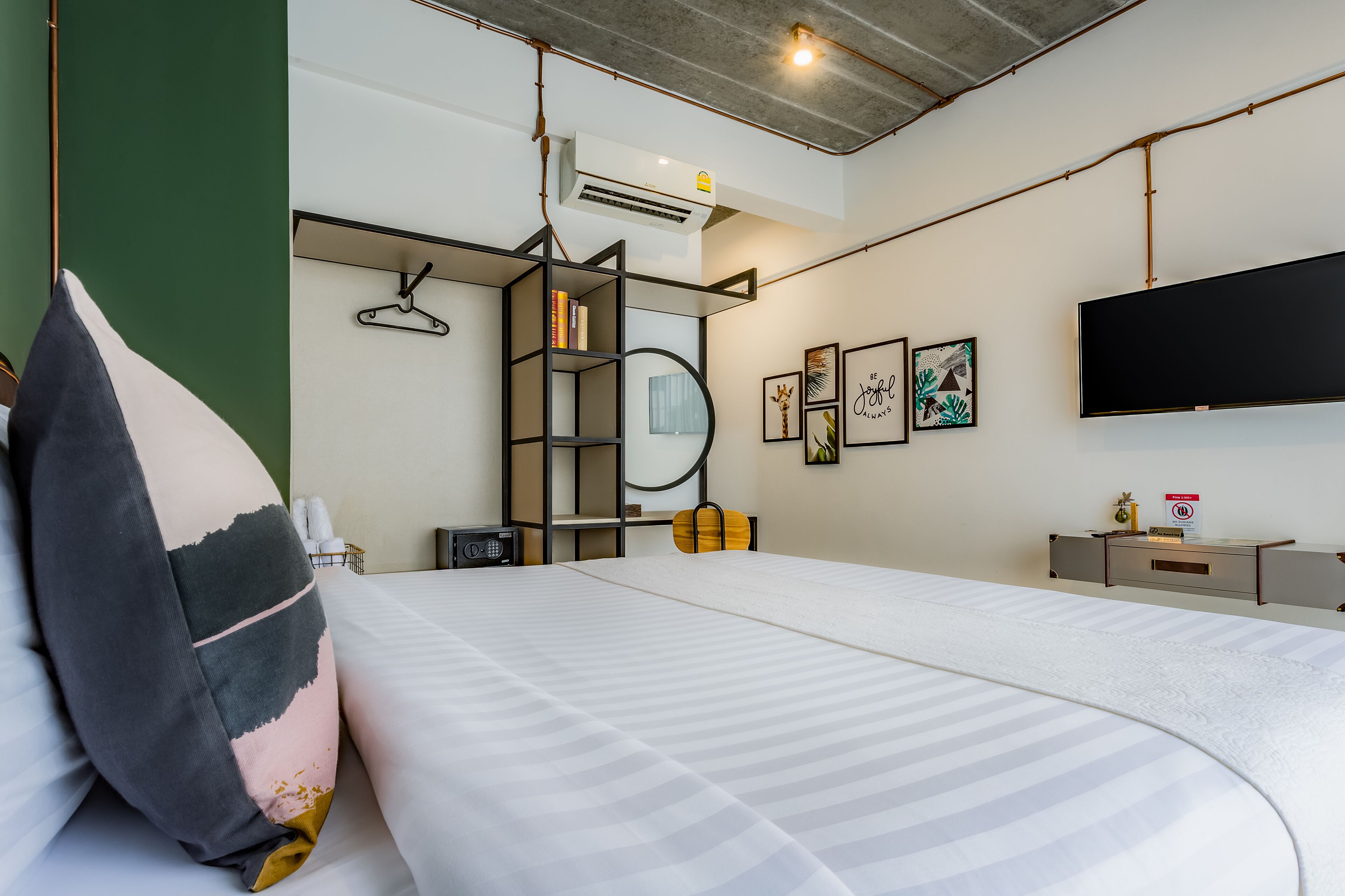 Une chambre d’hôtel moderne dotée d’un grand lit, d’un téléviseur fixé au mur, d’une bibliothèque et d’un climatiseur mural.