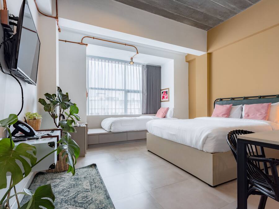 A modern bedroom with two beds, a desk, a chair, and a large window.