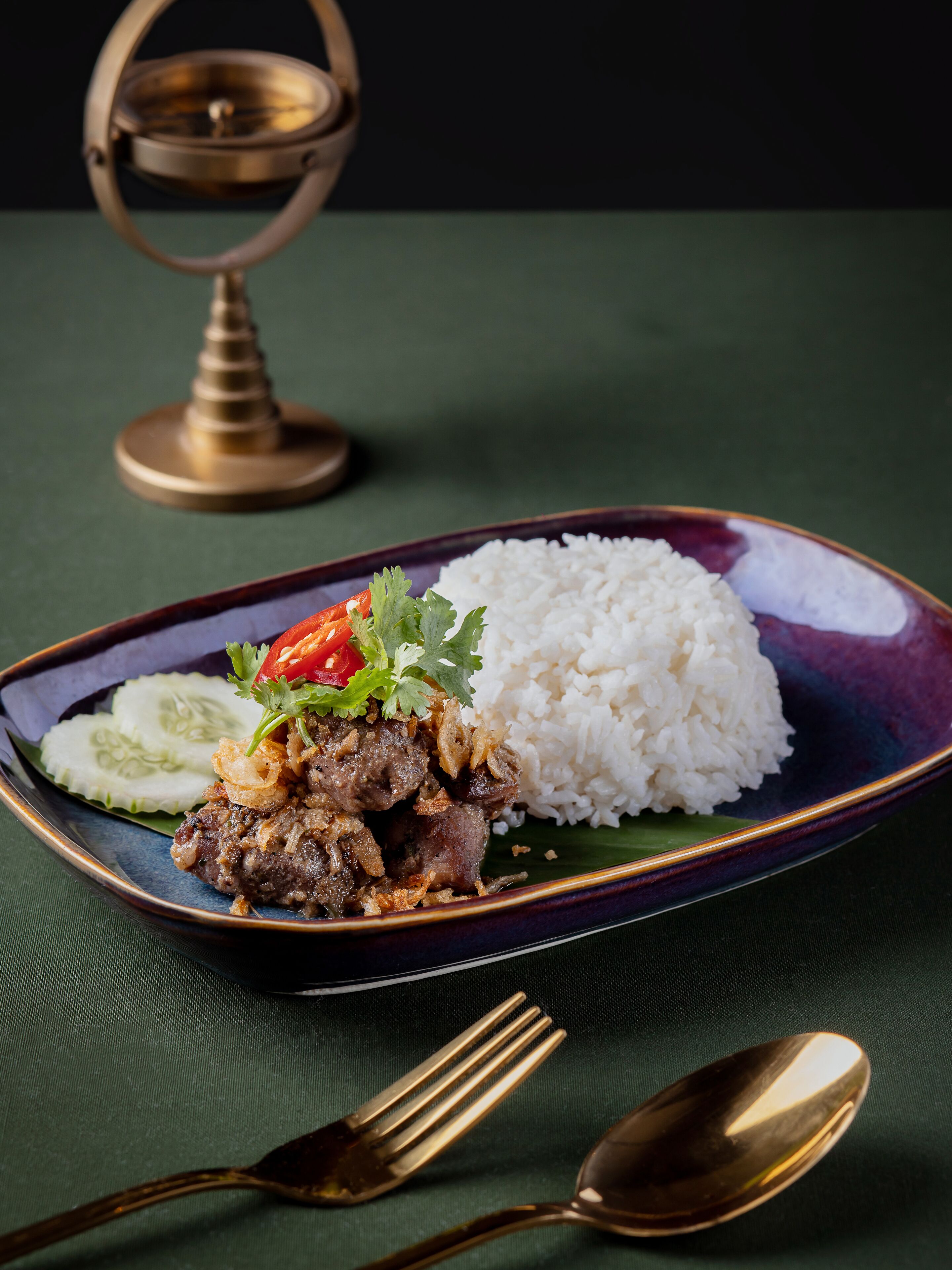 Un plato de arroz blanco, carne de res y vegetales sobre un mantel oscuro.