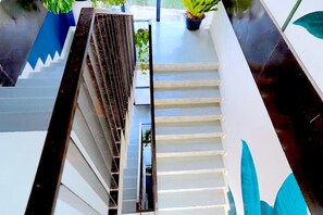 A modern staircase with white steps and a metal railing, leading to a landing area with potted plants. - The Wood (Surin)