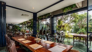 A spacious indoor dining area with large windows, wooden tables, and leather chairs. - The Wood (Surin)