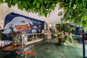 A lobby with a mural, a reception desk, and various plants. - The Wood (Surin)