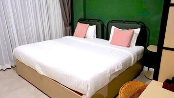 Una cama con ropa blanca y almohadas rosadas, una pared verde y una ventana con cortinas blancas.