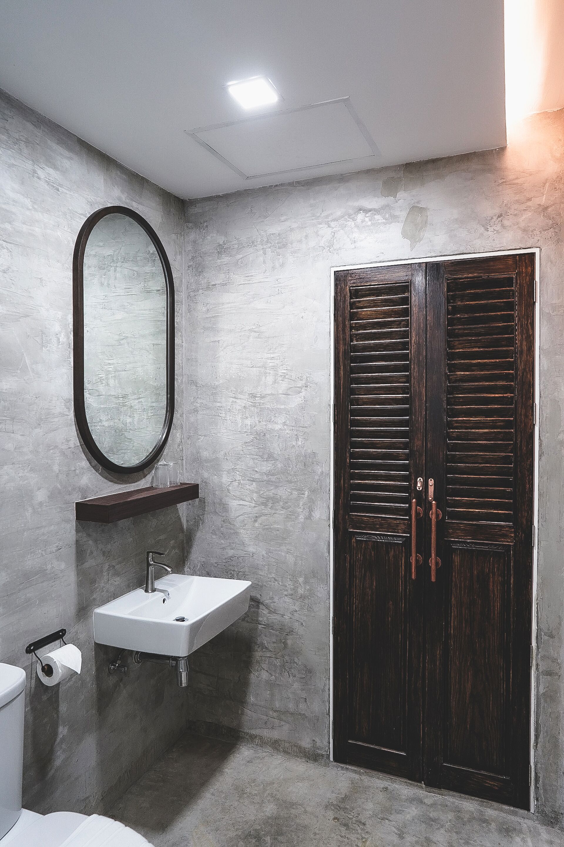 Un baño con un lavamanos rectangular, un espejo y una puerta de madera oscura.