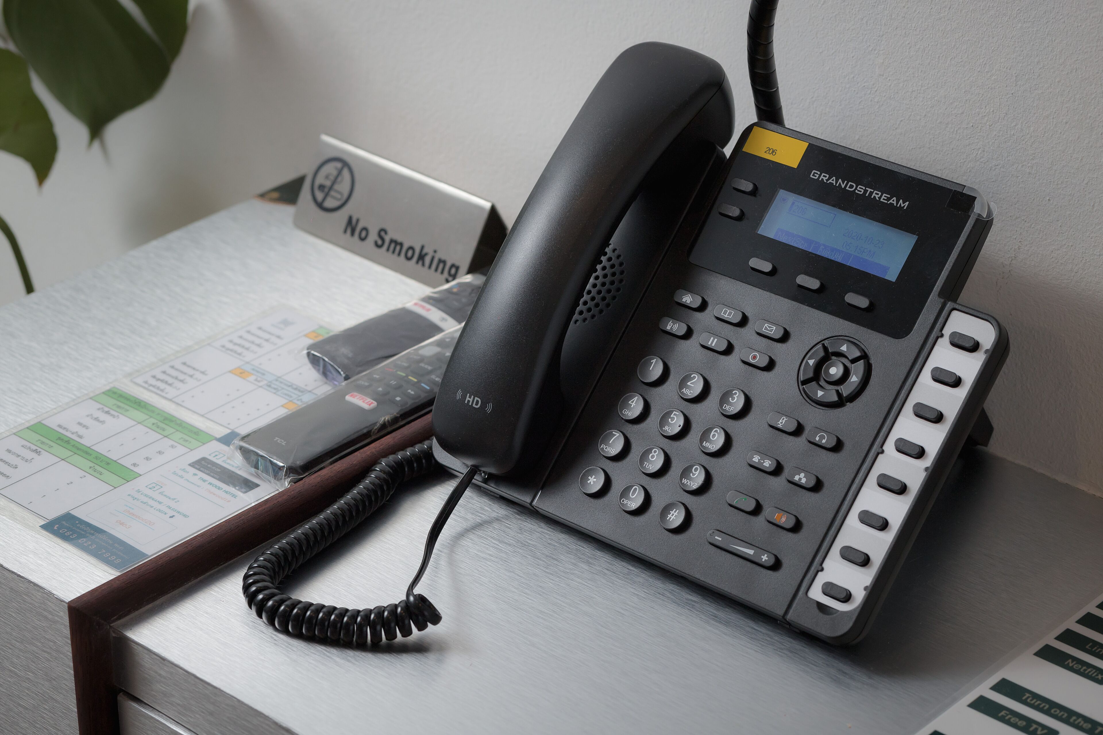 Um telefone Grandstream sobre uma mesa, com um aviso de 'Não Fumar' e um documento impresso.