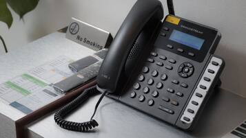 Um telefone Grandstream sobre uma mesa, com um aviso de 'Não Fumar' e um documento impresso.