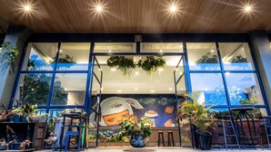 A modern building entrance with large windows, indoor plants, and a mural. - The Wood (Surin)