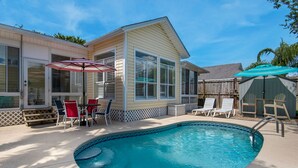 Un patio trasero con piscina, un porche cubierto y una terraza de madera.
