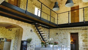 Una habitación amplia con pared de piedra, una escalera de madera y un entresuelo con lámparas colgantes.