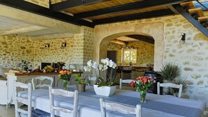 Una cocina rústica de piedra con techo de madera, una mesa de comedor con sillas blancas y una variedad de flores.