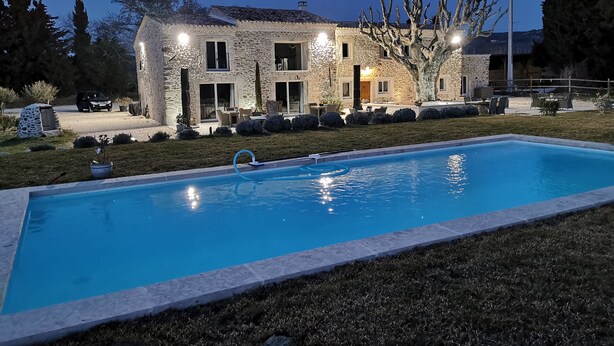 Una casa de piedra con piscina, mobiliario de exterior y un patio bien iluminado.