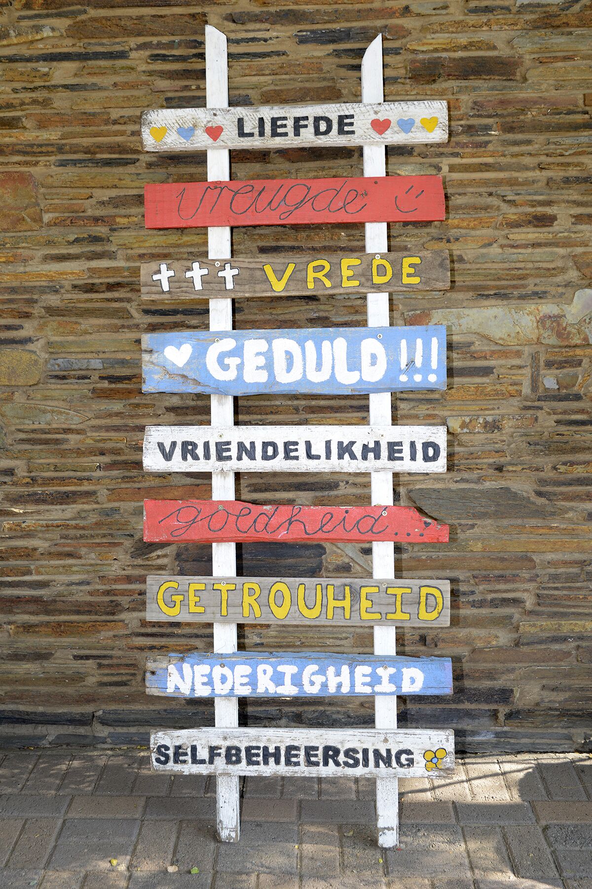 A wooden sign with various phrases in different colors and fonts, mounted on a brick wall.