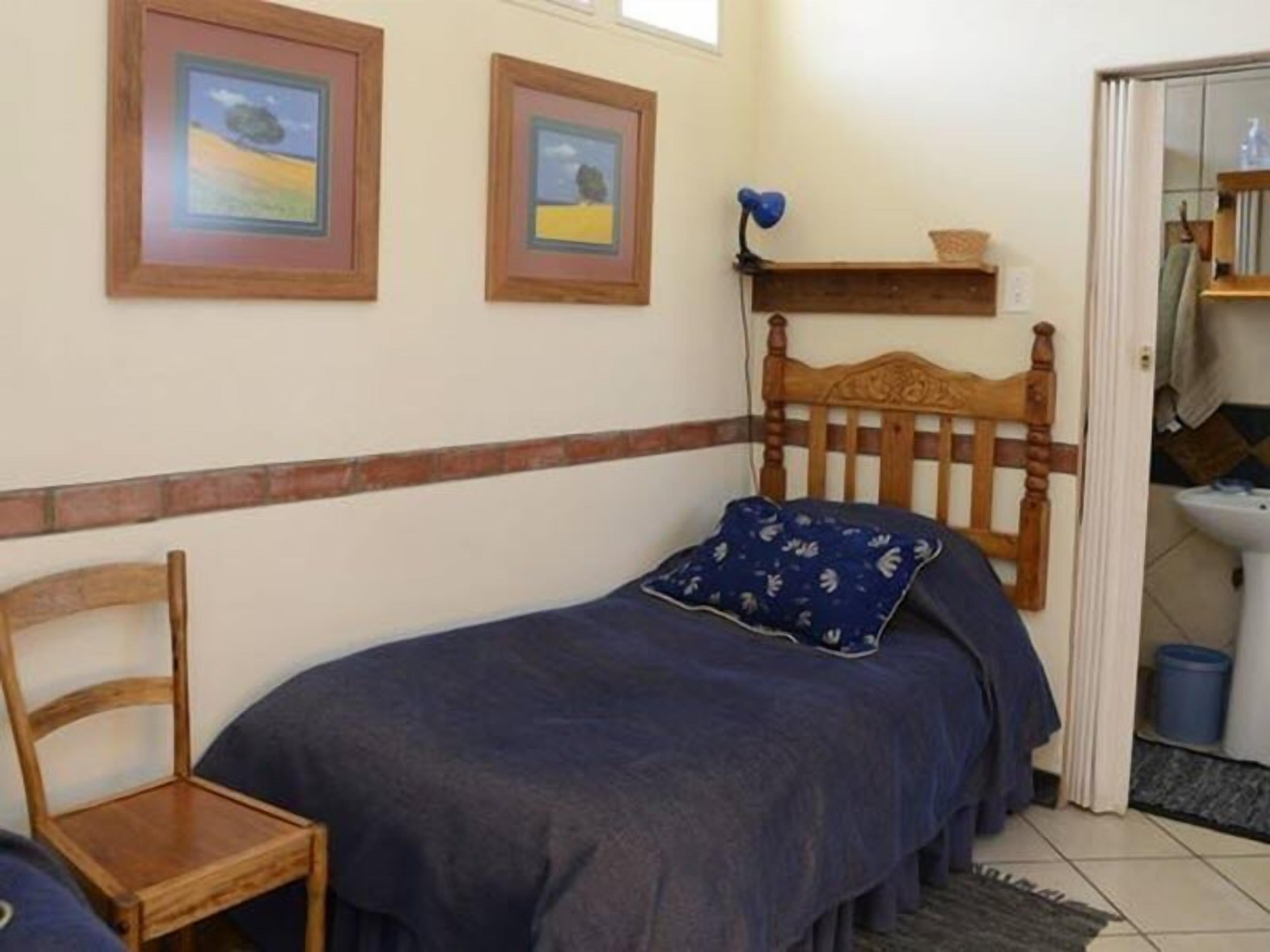 Una habitación pequeña y acogedora con una cama individual, una silla de madera y dos cuadros en la pared.