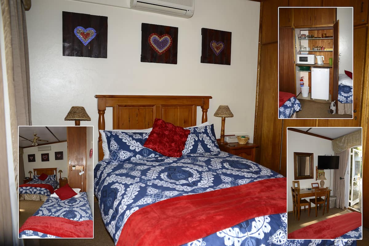 A bedroom with a large bed, two bedside tables, a wooden headboard, and a small kitchenette.