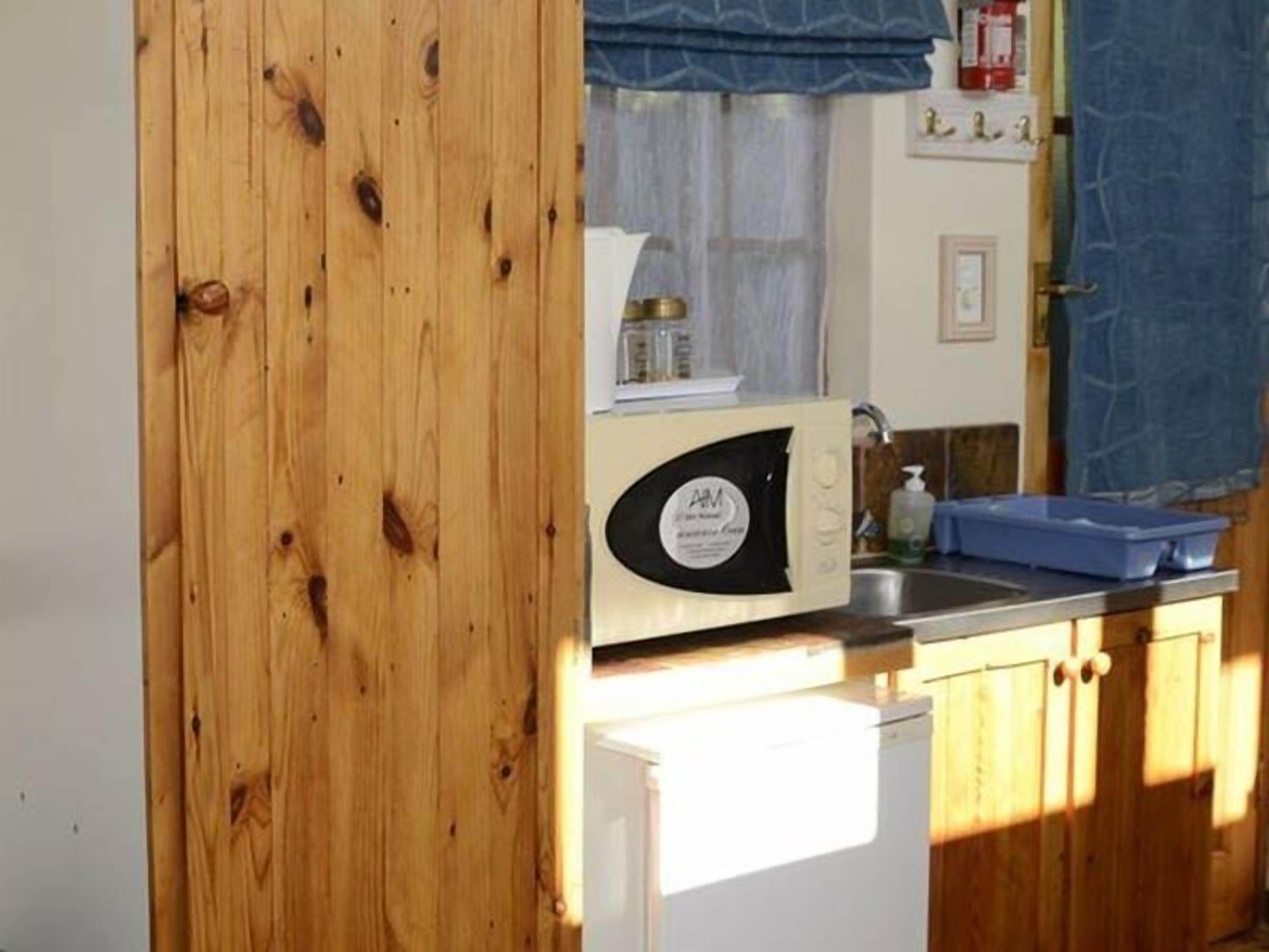 Una cocina compacta con armarios de madera, un microondas, un refrigerador pequeño y un lavamanos.