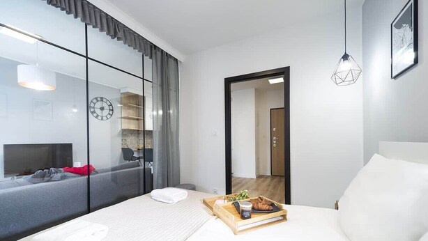 Une chambre d'hôtel moderne avec un grand lit, une table de chevet sur laquelle se trouve un plateau de petit-déjeuner, une télévision et une grande fenêtre avec des rideaux.