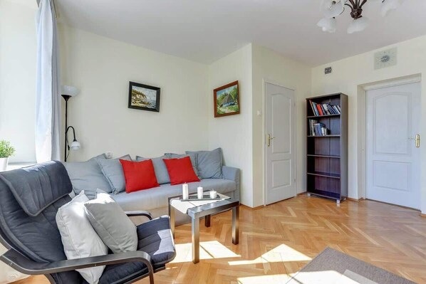 Una sala de estar con un sofá gris, cojines rojos, una mesa de centro y una estantería.