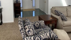 A spacious living room with a large sofa, a coffee table, and a beige couch. There is a door leading to another room and a small table with a lamp. - A Den for all four seasons, visit the Bear's Den and create lasting memories. (McGaheysville)