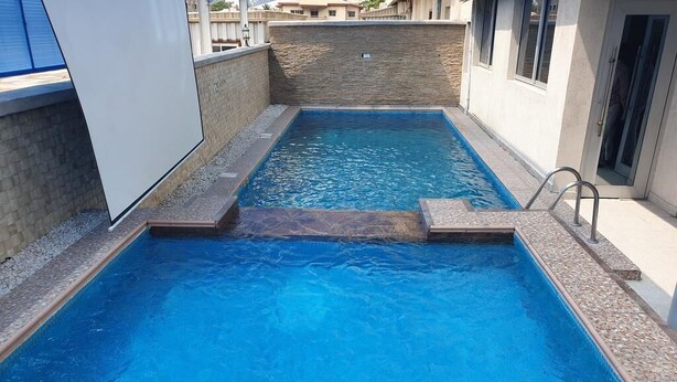 Una piscina rectangular amb una petita cascada, envoltada per una paret de pedra i una escala metàl·lica.