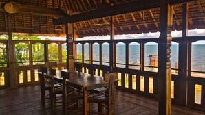 A wooden interior with a table and chairs, large windows with a view of the sea, and a ceiling fan. - LooLa Adventure Resort (Bintan)