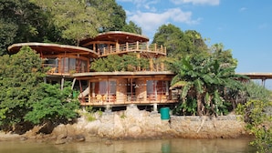 A multi-level wooden cabin with balconies, situated by a body of water, surrounded by lush greenery. - LooLa Adventure Resort (Bintan)