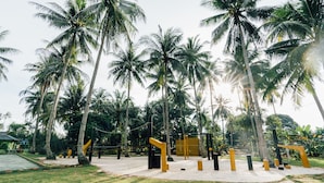 A playground with yellow and black equipment, surrounded by tall palm trees. - LooLa Adventure Resort (Bintan)