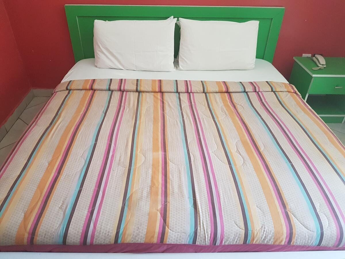 A bed with a striped bedspread, a green headboard, and a green nightstand with a telephone.