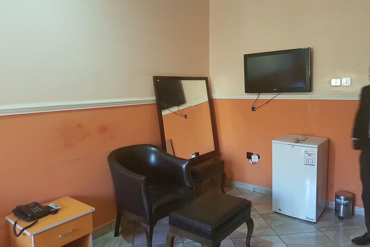 A room with a leather chair, a small table with a phone, a television on the wall, and a refrigerator.