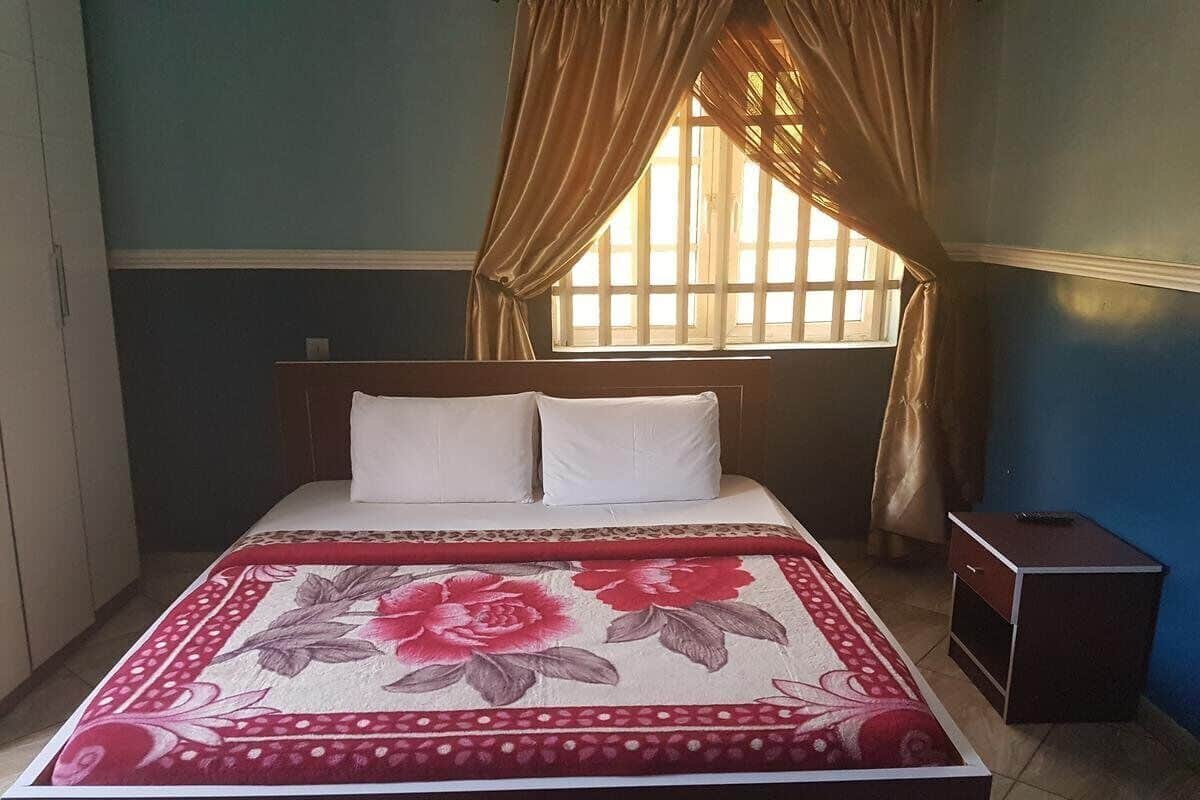 A bedroom with a bed, a nightstand, and a window with curtains.
