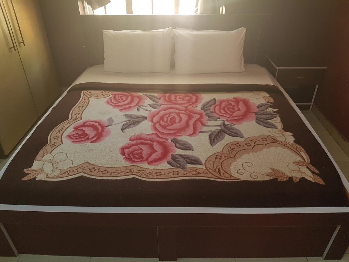 Una cama con un edredón estampado con flores, una almohada blanca y una mesita de noche con una lámpara.