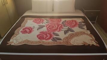 Una cama con un edredón estampado con flores, una almohada blanca y una mesita de noche con una lámpara.