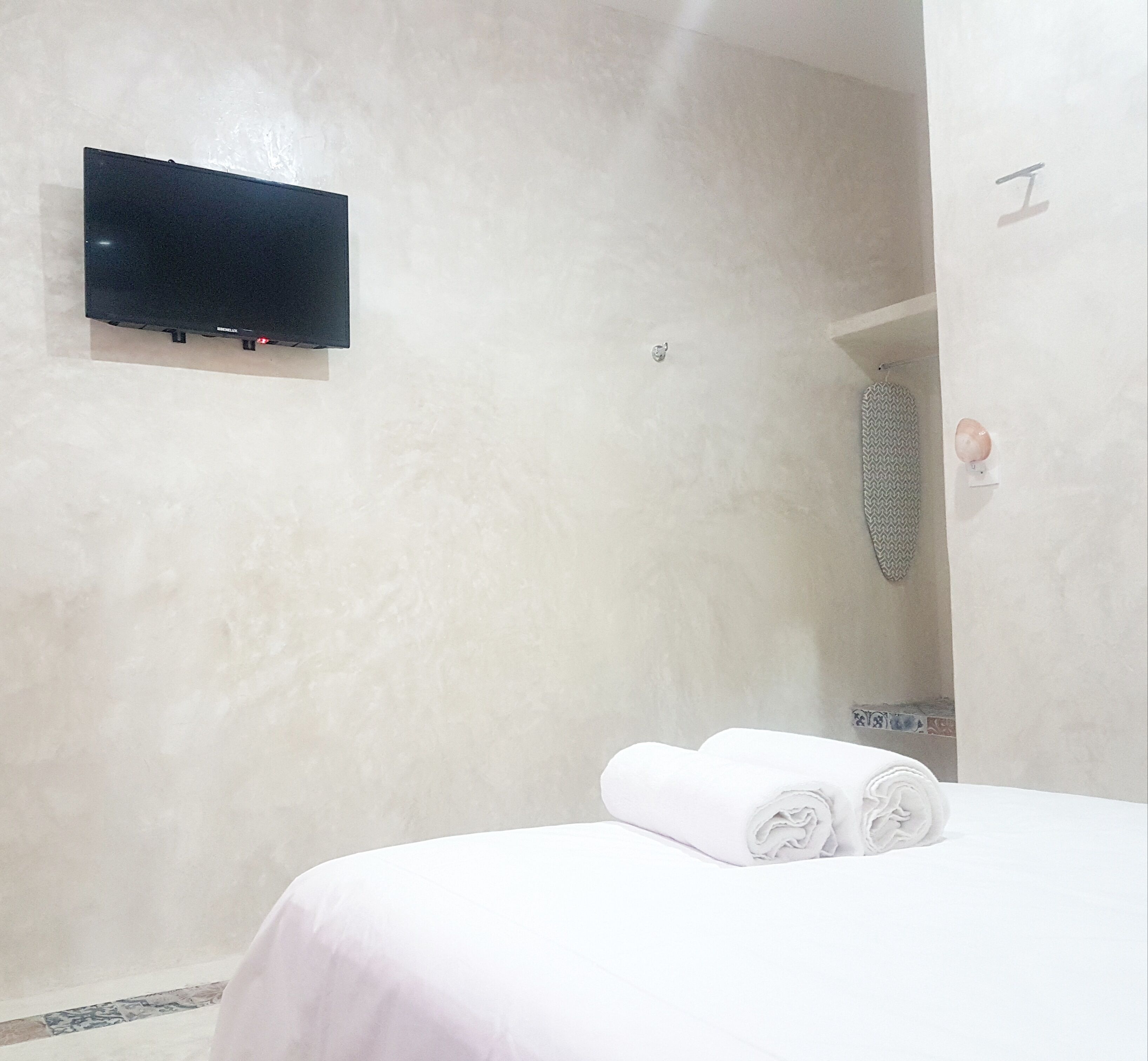 Habitación de hotel con cama, televisión montada en la pared y zona de ducha.
