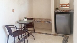 A small room with a round table and two chairs, a refrigerator, and a shelf with a mirror. - Casa Chujuk by Spirit Group (Isla Holbox)