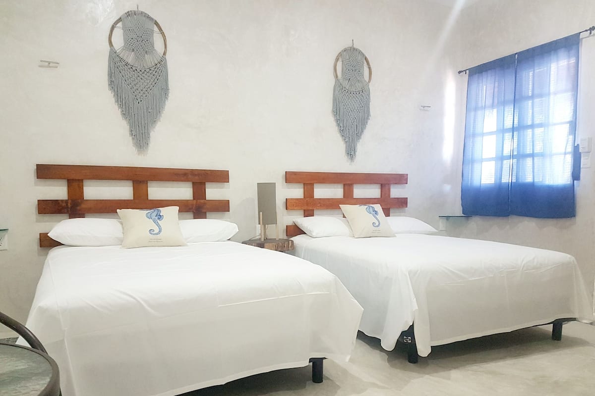 Une chambre avec deux lits, des têtes de lit en bois, du linge de lit blanc et des éléments décoratifs accrochés aux murs.