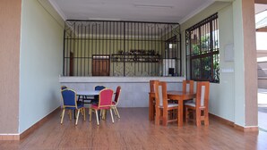 A dining area with a table and chairs, a window with metal bars, and a shelf with bottles. - Panone Hotel Chekereni (Arusha)