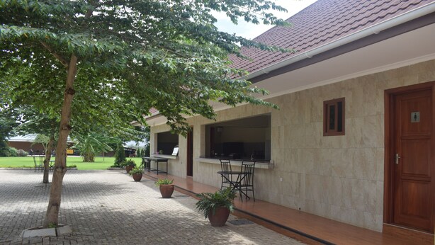 A courtyard with a tiled floor, potted plants, a tree, and a building with a tiled roof and a door. - Panone Hotel Chekereni (Arusha)