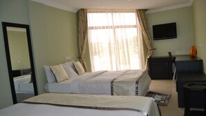 A hotel room with two beds, a desk, a chair, a TV, and a window with curtains. - Panone Hotel Chekereni (Arusha)