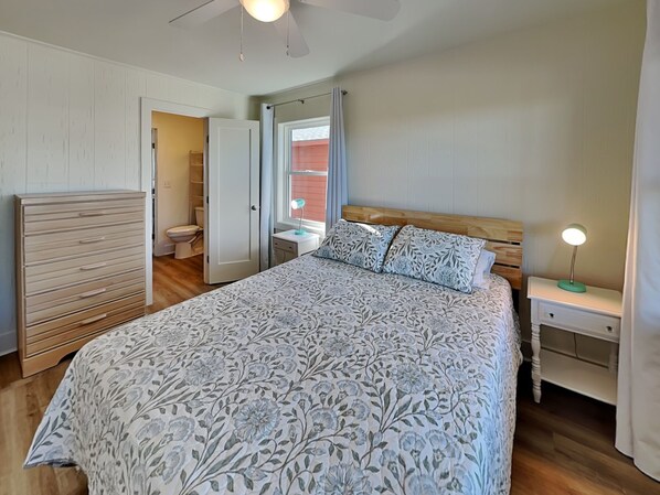 A bedroom with a bed, bedside tables, a wardrobe, a ceiling fan, and a bathroom visible through an open door. - Walking On Sunshine-Dolphin Level | Ocean Views! (Holly Ridge)