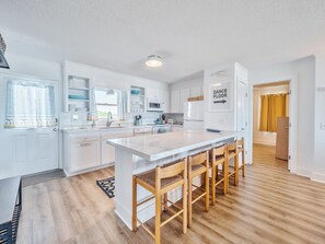 A modern kitchen with white cabinetry, a large island with bar stools, and a sign indicating a dance floor. - Walking On Sunshine-Dolphin Level | Ocean Views! (Holly Ridge)