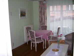 Uma área de refeições com mesa posta para dois, duas cadeiras, um radiador e uma janela com cortinas.