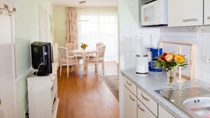 A compact kitchen with a microwave, a coffee maker, and a sink. There is a dining area with a table and chairs, and a vase with flowers on the counter.