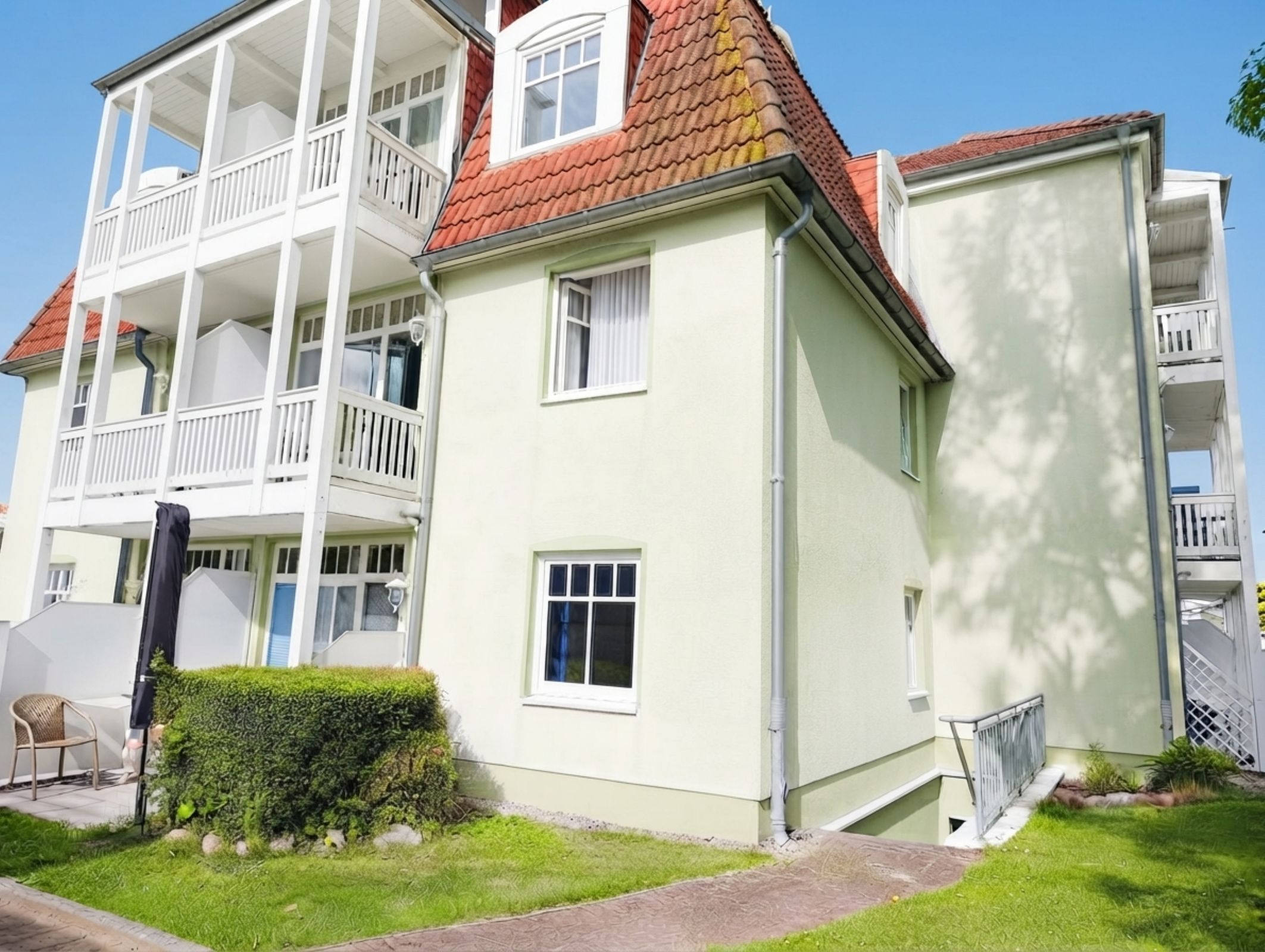 A multi-story residential building with balconies, a garden area, and a pathway leading to the entrance.