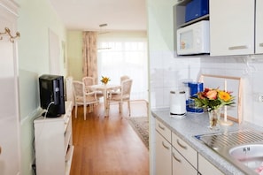 A compact kitchen with a microwave, a coffee maker, and a sink. There is a dining area with a table and chairs, and a vase with flowers on the counter.