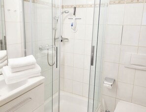 A modern bathroom with a glass-enclosed shower, a toilet, and a sink area.
