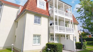 Un immeuble résidentiel à deux étages, doté d’un toit recouvert de tuiles rouges, de murs extérieurs blancs et d’un balcon à l’étage supérieur.